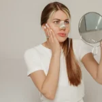 a young woman with a bandage on her nose after rhinoplasty with a mirror in her hand