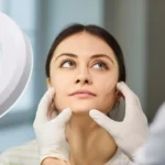 woman esthetician examining face of patient under lamp magnifier