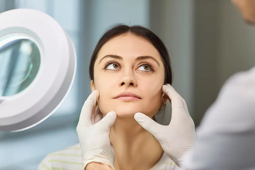 woman esthetician examining face of patient under lamp magnifier